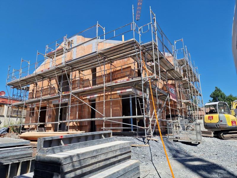 Ziegelrohbau mit Gerüst und Bagger auf der Baustelle